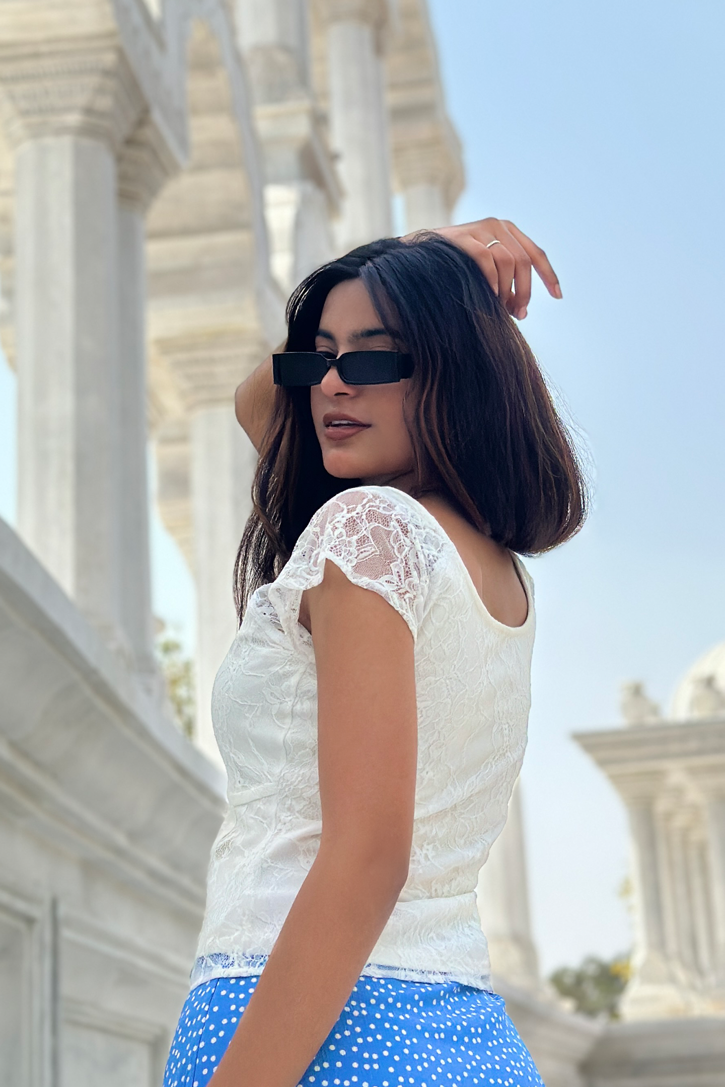 A woman models a Ronazen white lace top featuring delicate floral patterns. The top has short, scalloped sleeves and a soft, rounded neckline, emphasizing a gentle, feminine aesthetic. The fabric's semi-sheer quality adds a touch of elegance and sophistication, while the fitted silhouette provides a flattering fit. The background is neutral to highlight the intricate details of the lace
